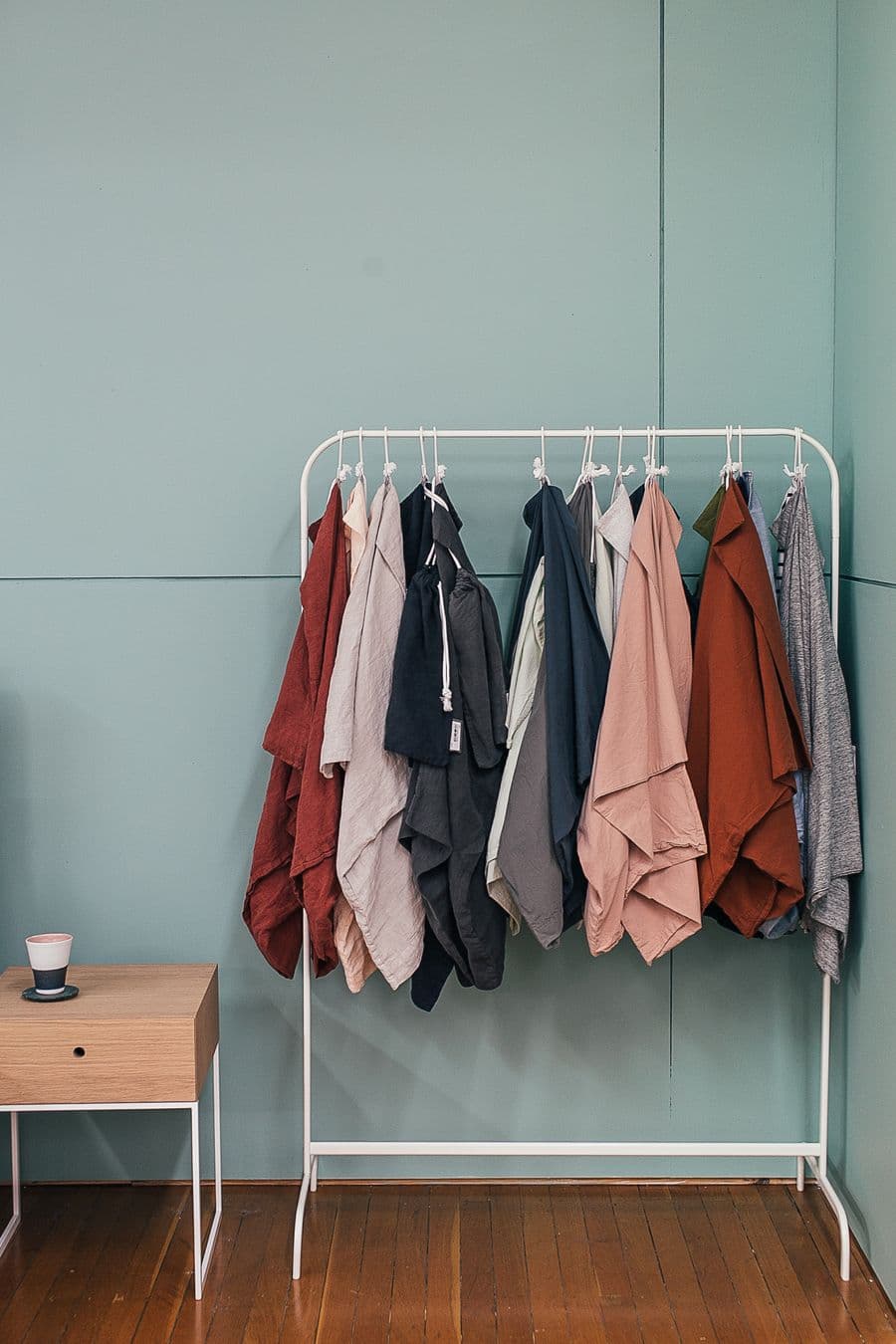 Clothes hanging on a white rail against a soft green wall