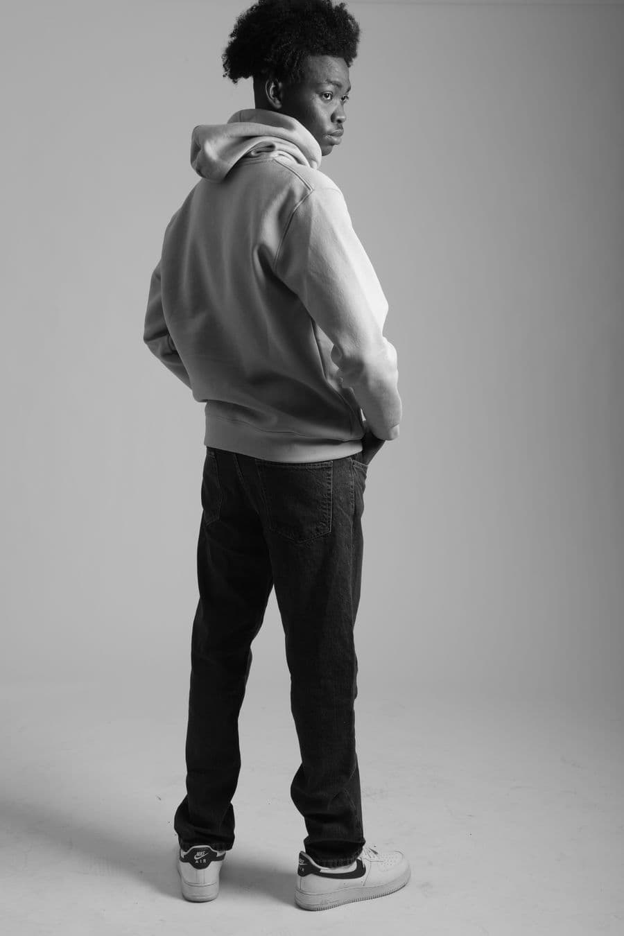 A person in a grey hoodie seen from behind, studio backdrop