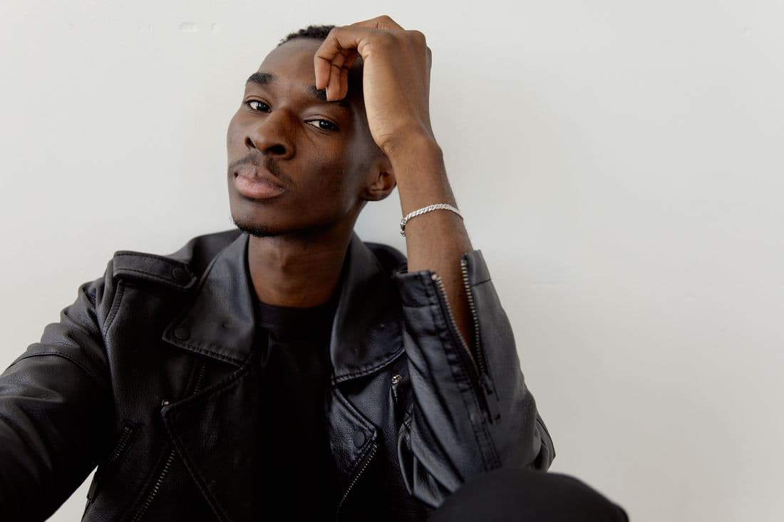 A man in a black jacket against a white wall